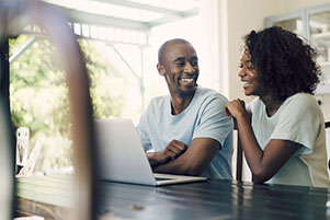 A photo of happy couple using laptop at home. Cheerful man sitting with woman at table.