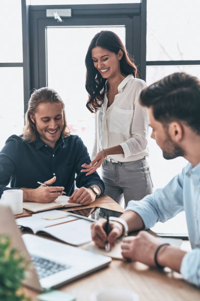 Young modern colleagues in smart casual wear working together and smiling while spending time in the office