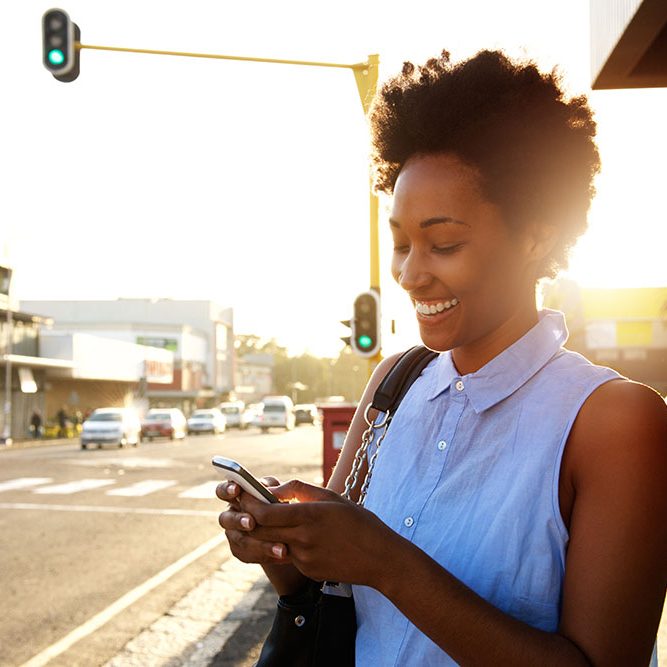 Close up portrait of beautiful young african woman using cellphone outdoors in the city